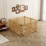 Light wood square dog playpen with vertical slats in bright room, small pet inside, herringbone floor, wall art, and side table.