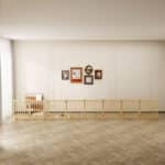 Light wood six-panel dog fence with vertical slats used as indoor room divider, two small dogs inside, bright room with framed art.