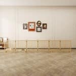 Light wood eight-panel dog fence with vertical slats used as indoor pet barrier in bright room with herringbone floor and wall art.