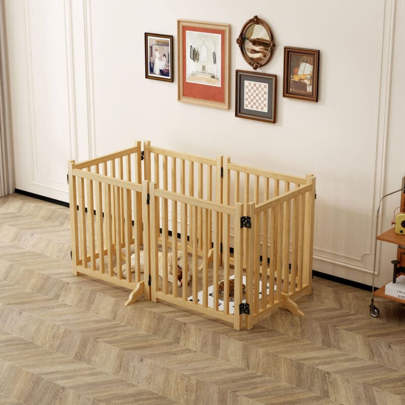 Light wood rectangular dog playpen with vertical slats, two small dogs inside, in a bright modern room with framed wall art.